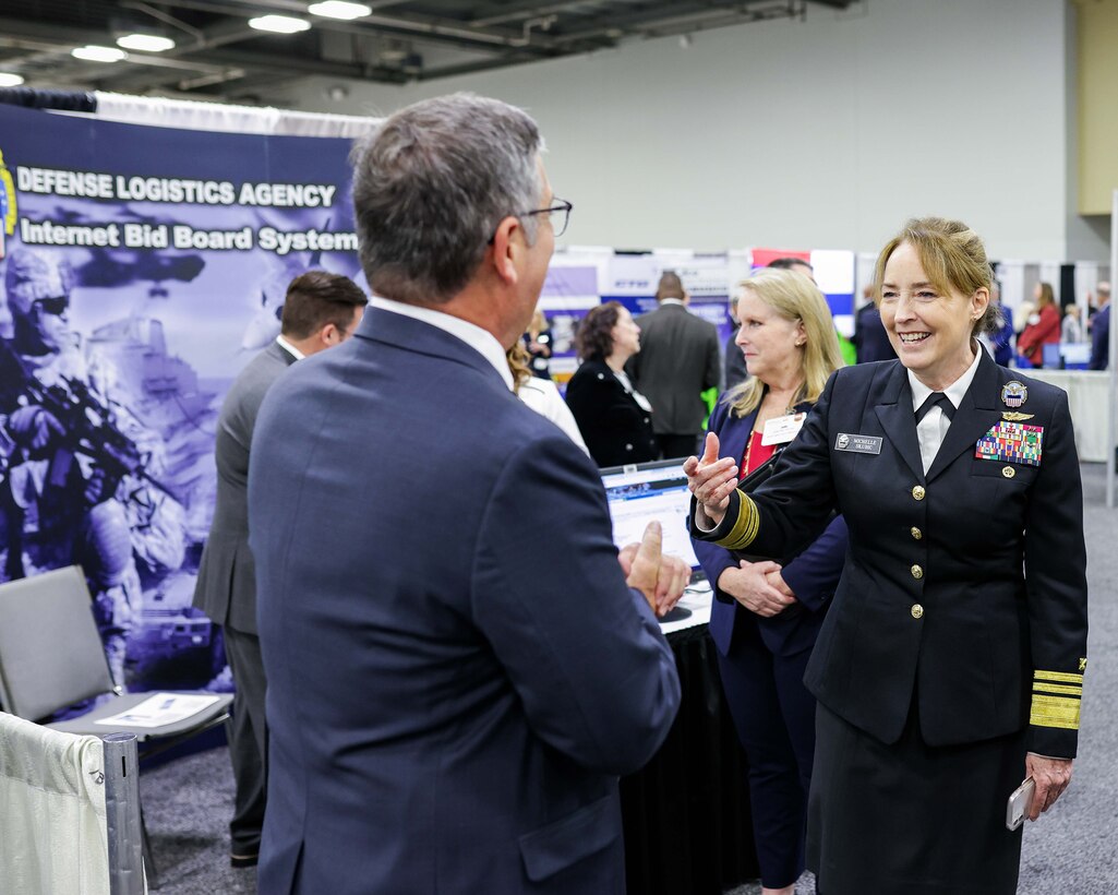 Woman in military uniform greets a man in a suit at a exhibition.