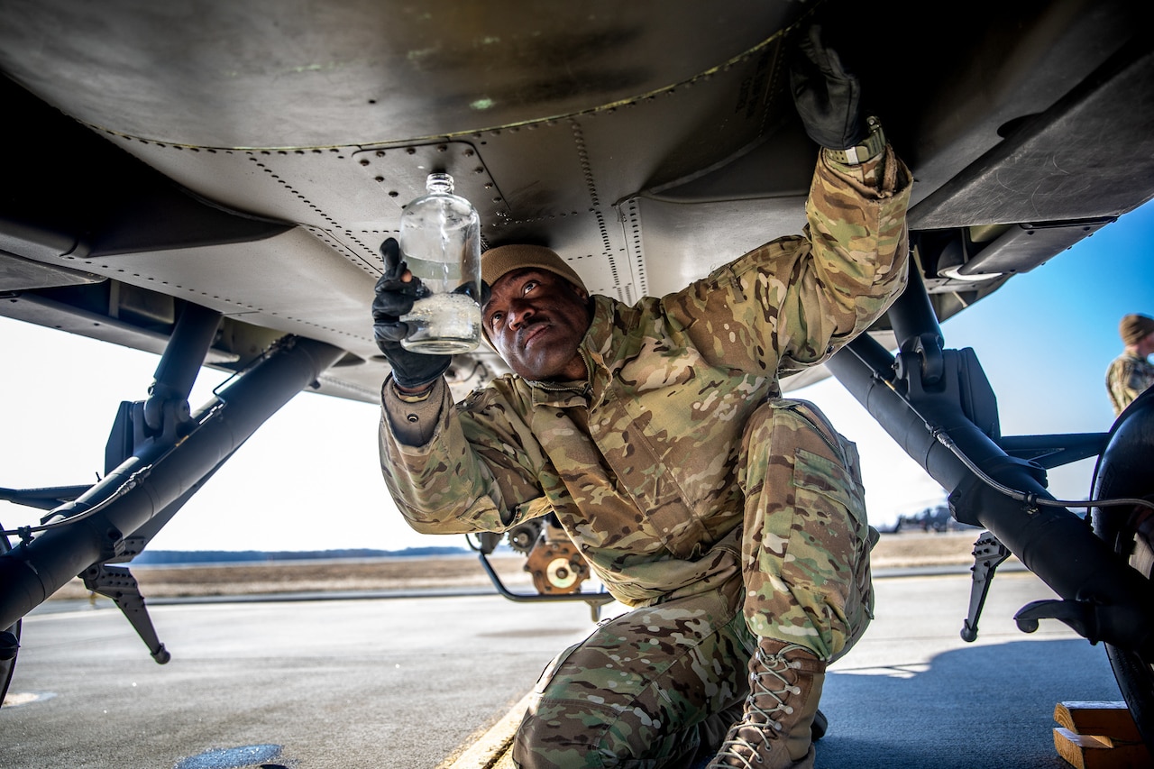 A soldier holds a bottle under an aircraft.