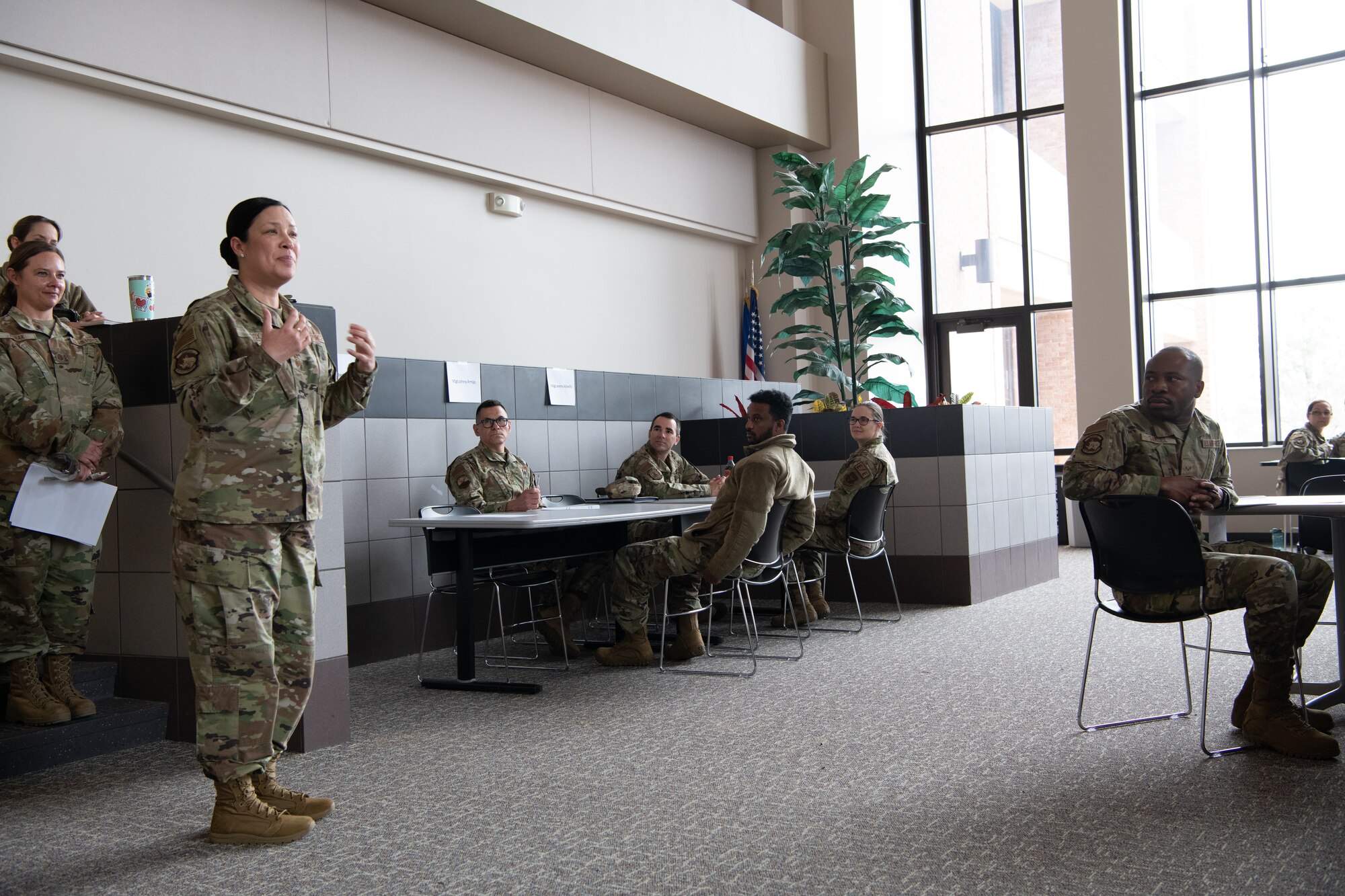 A woman speaks to a small audience in a room with large windows.