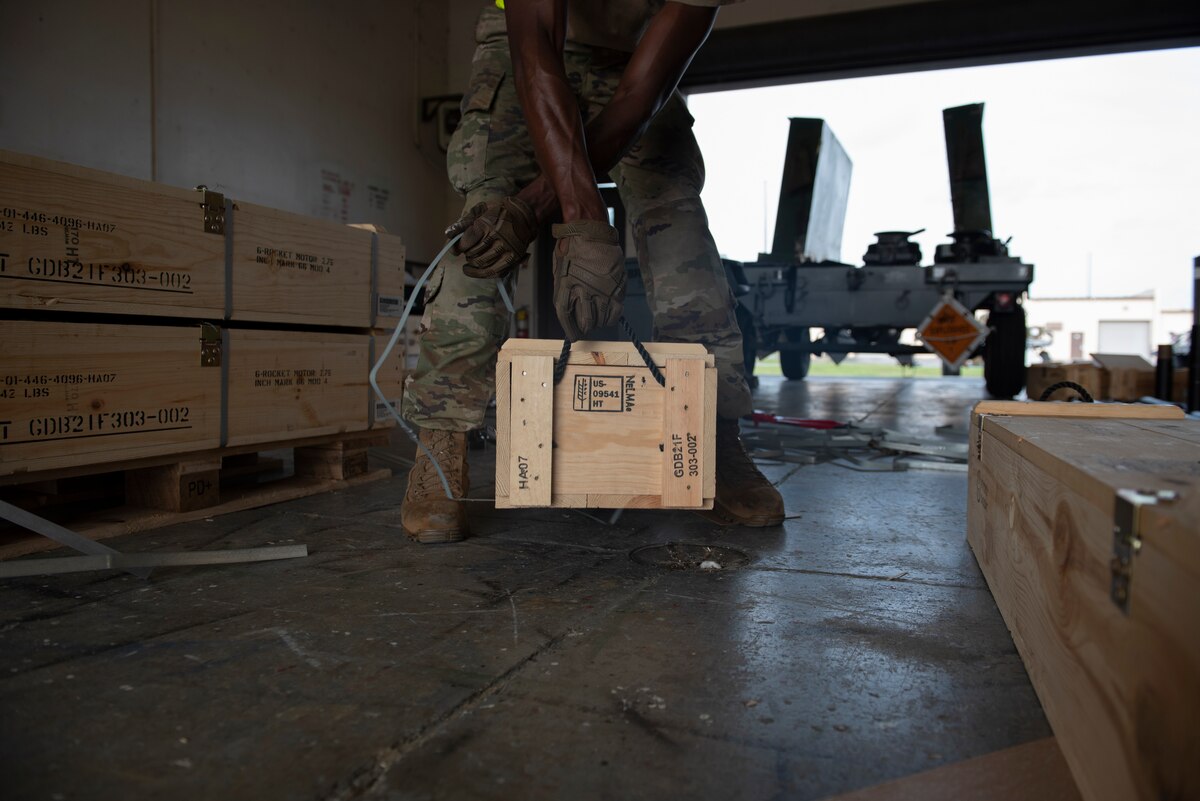 A photo of a person picking up a large box by the strap handle.