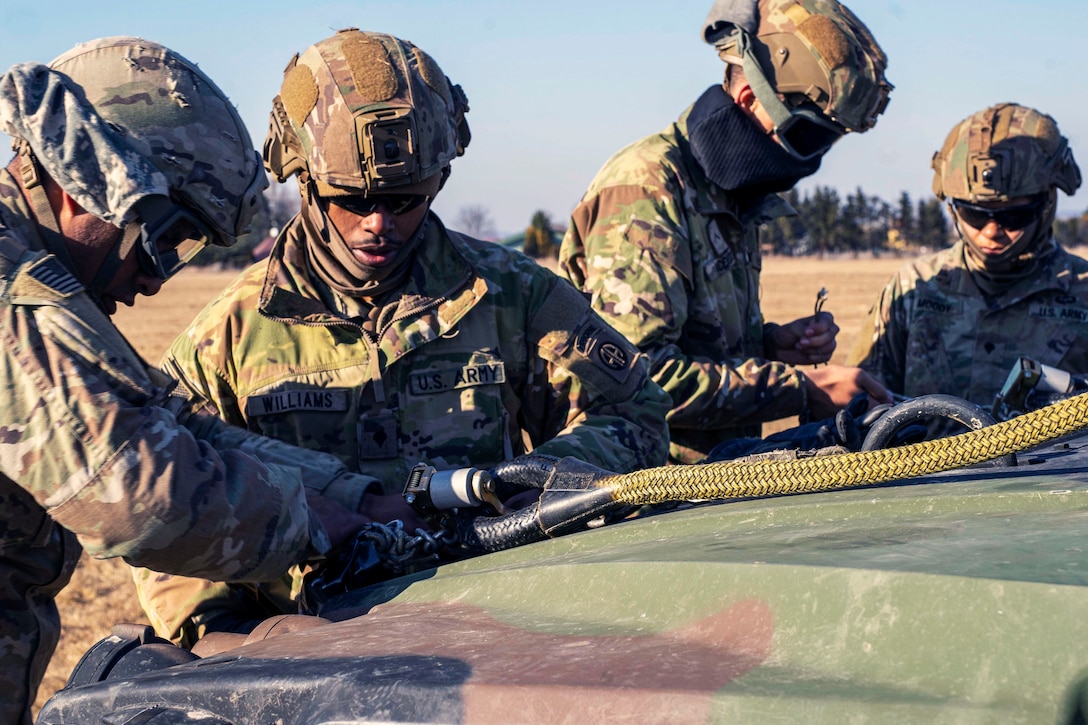 Four Marines latch cable lines on the hood of a military vehicle.