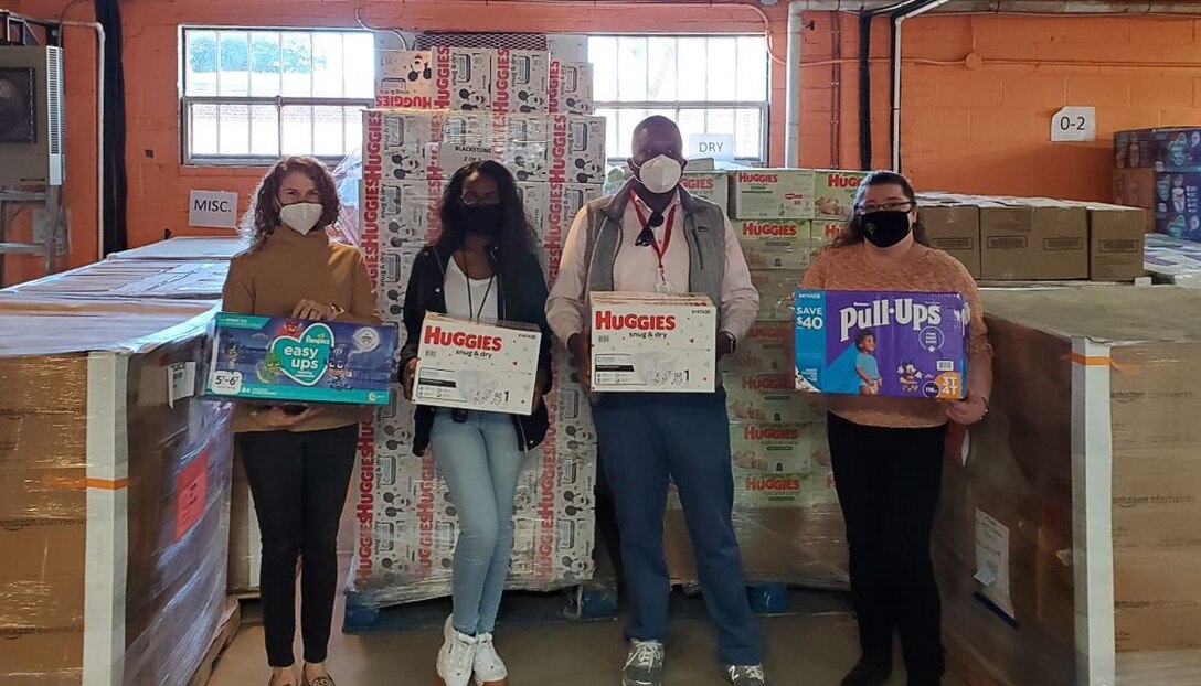 Four people hold boxes of supplies with other boxes of supplies near them.