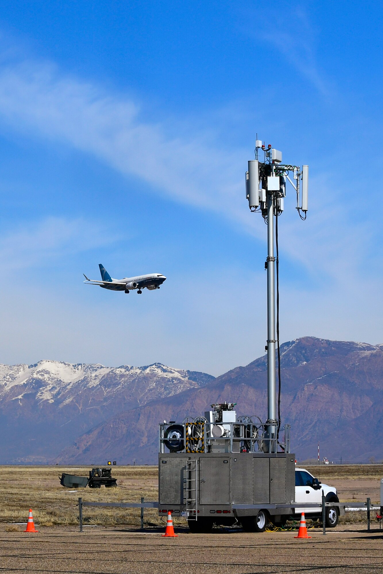 A Boeing 737 flies over the top of a mobile test station antennae with the Wasatch Mountains in the background.