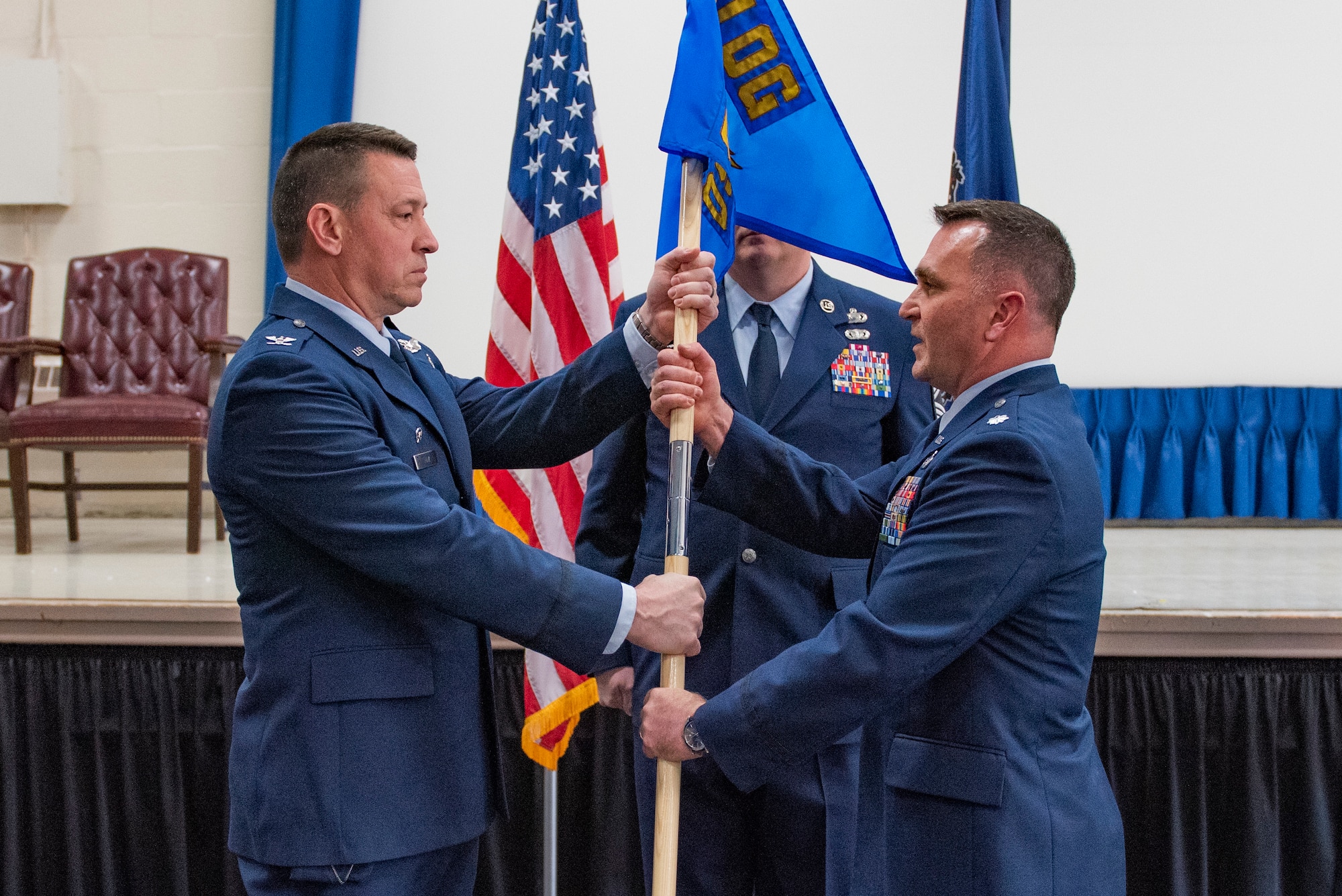 A man in Air Force dress blues takes a flag from another man in Air Force dress blues.