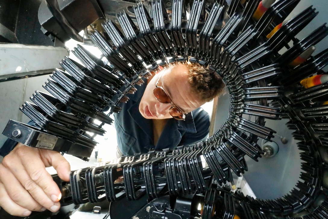 A sailor loads ammunition into machine gun aboard a ship at sea.