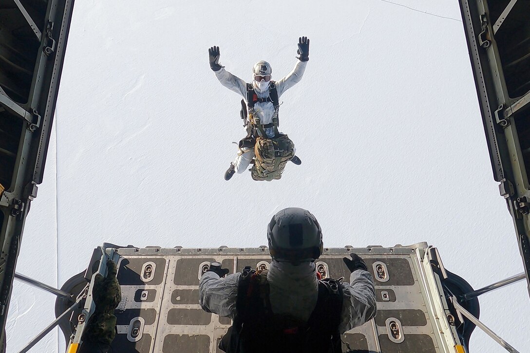 A man jumps out of an aircraft with snow-covered ground in the background.