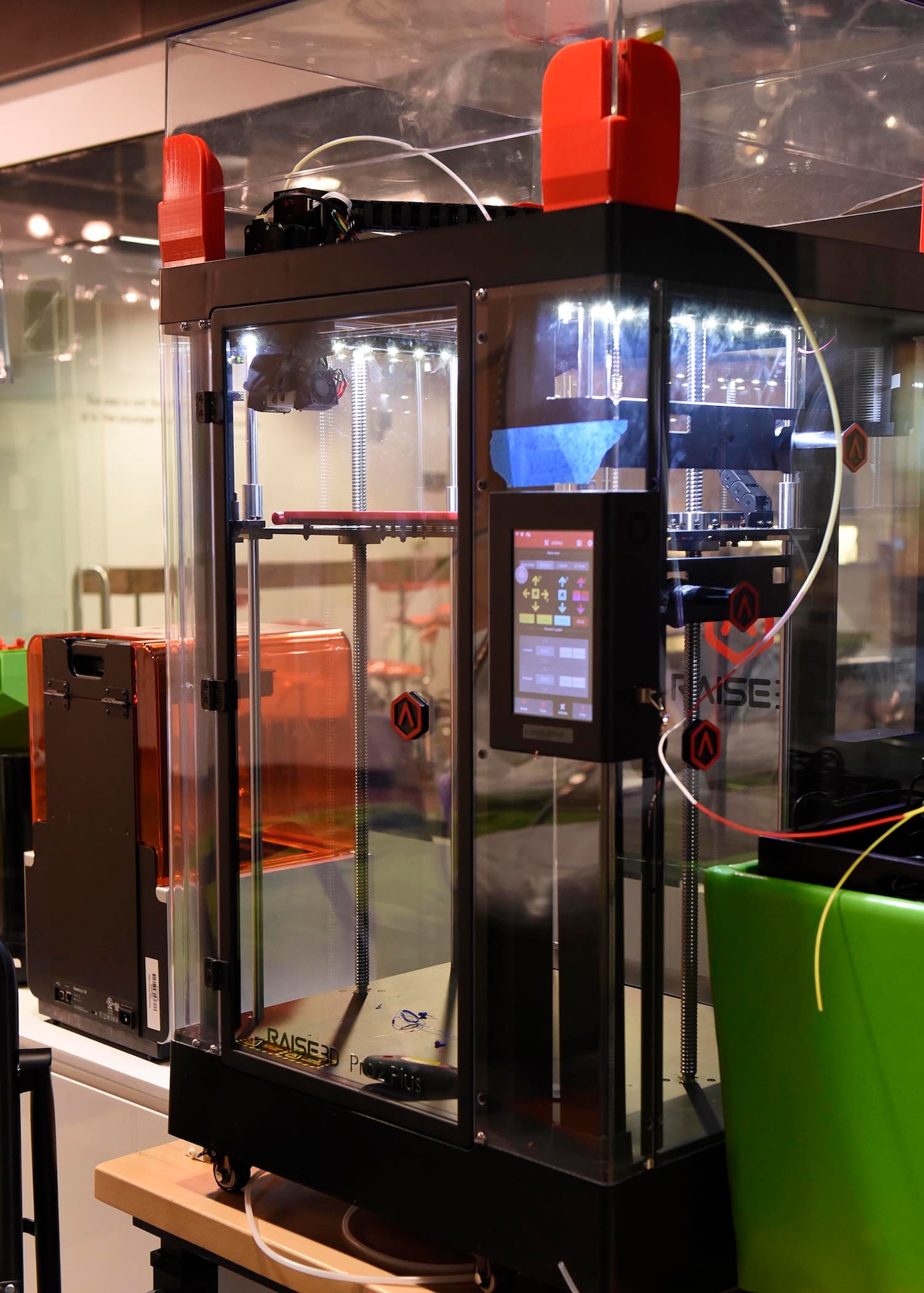 A black and red 3-D printer sits on top of a table ready for use.