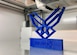 A blue 3-D model of Air Force wings print inside of a 3-D printer.