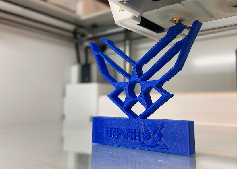 A blue 3-D model of Air Force wings print inside of a 3-D printer.