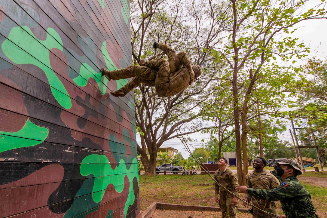 Two soldiers rappel down a wall as other watch.