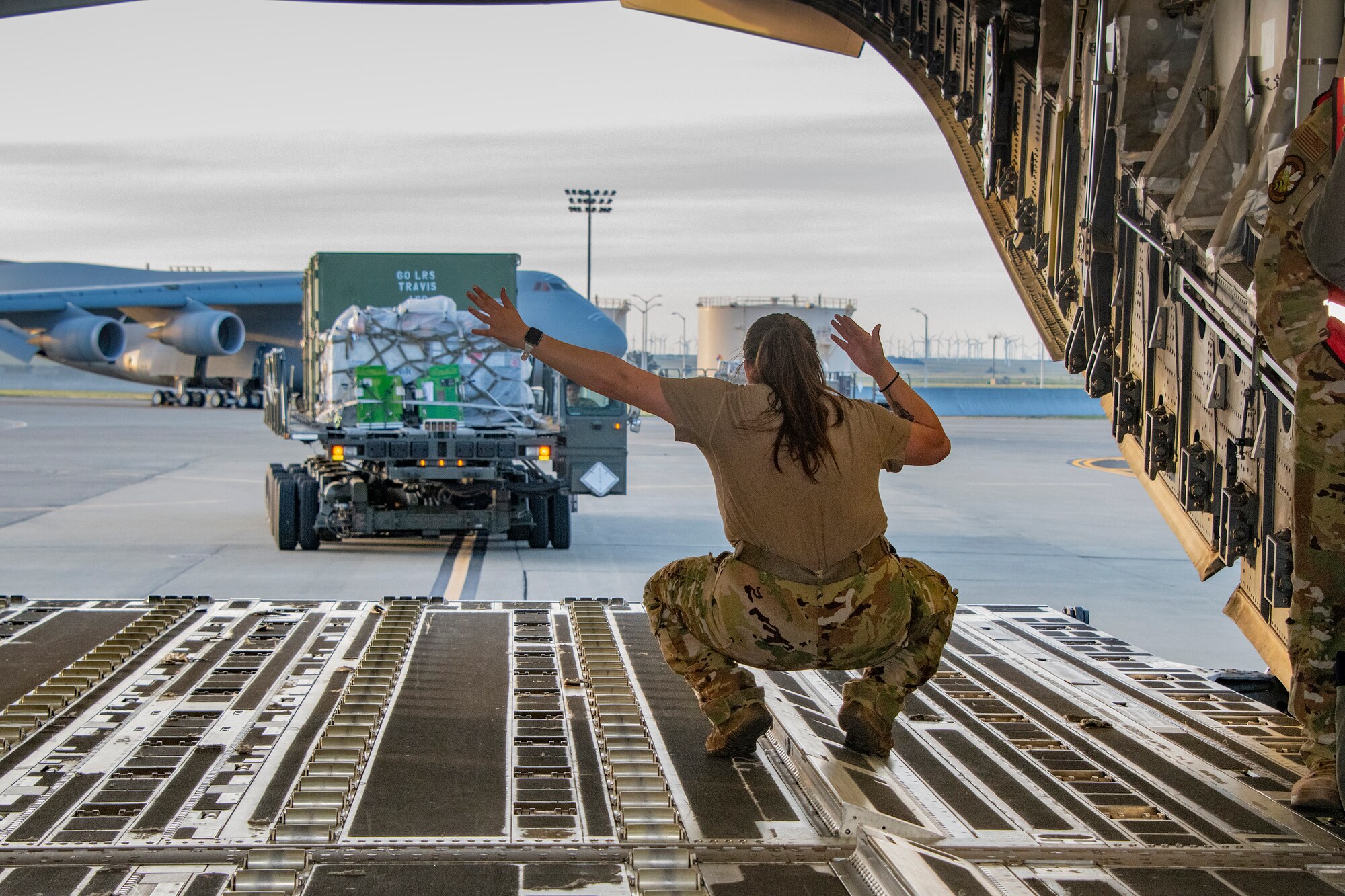 an airman directs a large military vehicle with pallets moves pallets into an airplane
