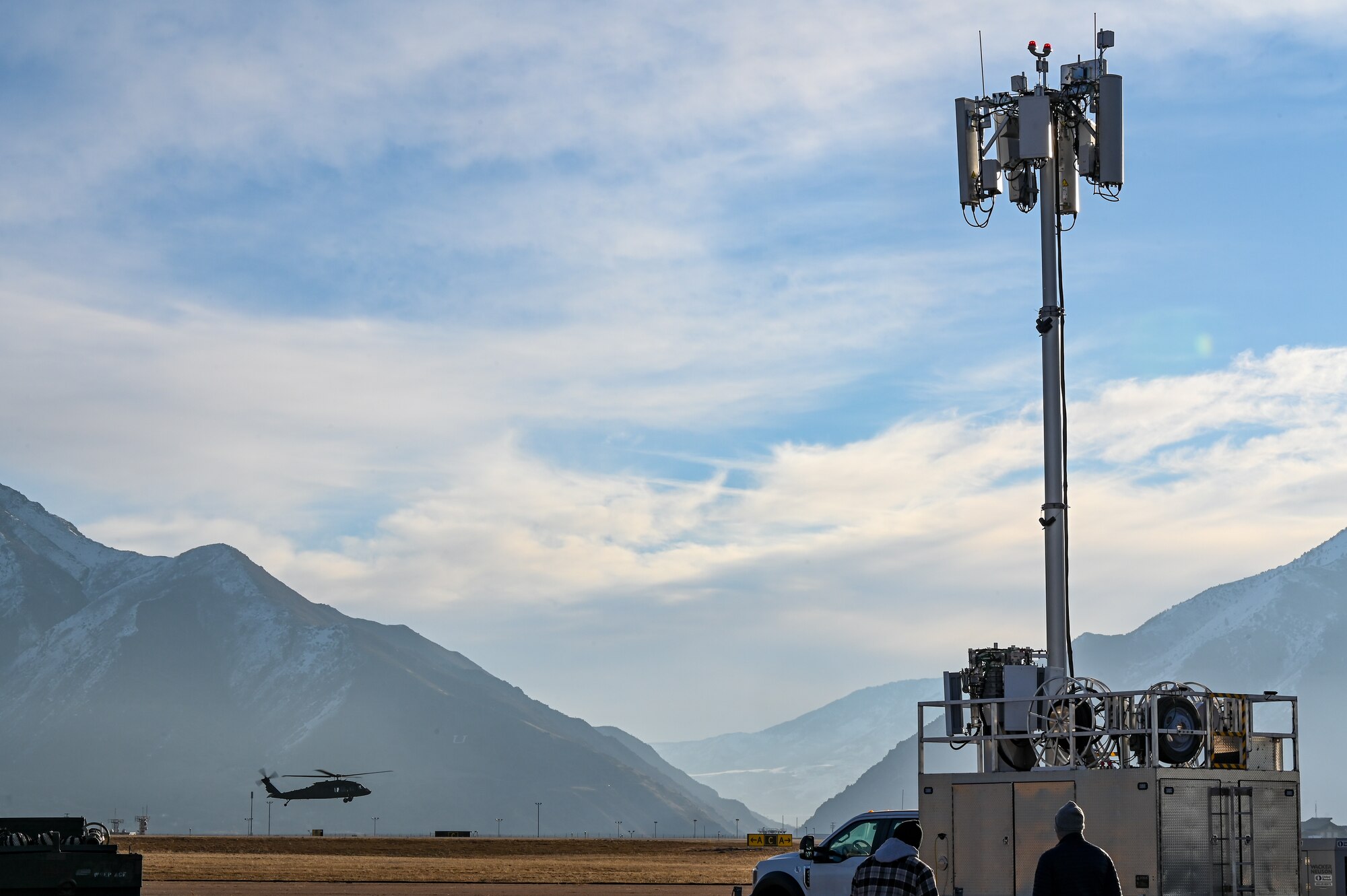 An UH-60 Blackhawk flies multiple passes at different altitudes over the runway with a mobile test station in the foreground.