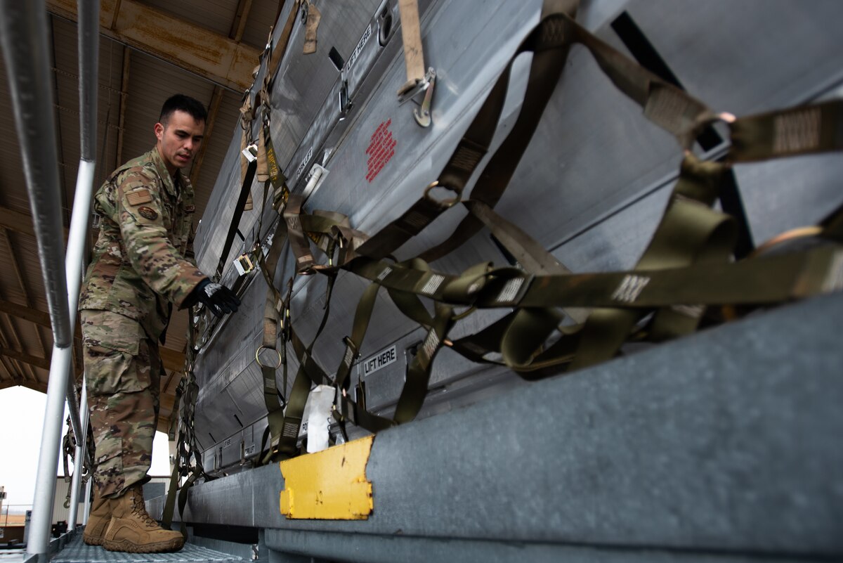 A military service member adjusts a strap on a pallet of equipment.