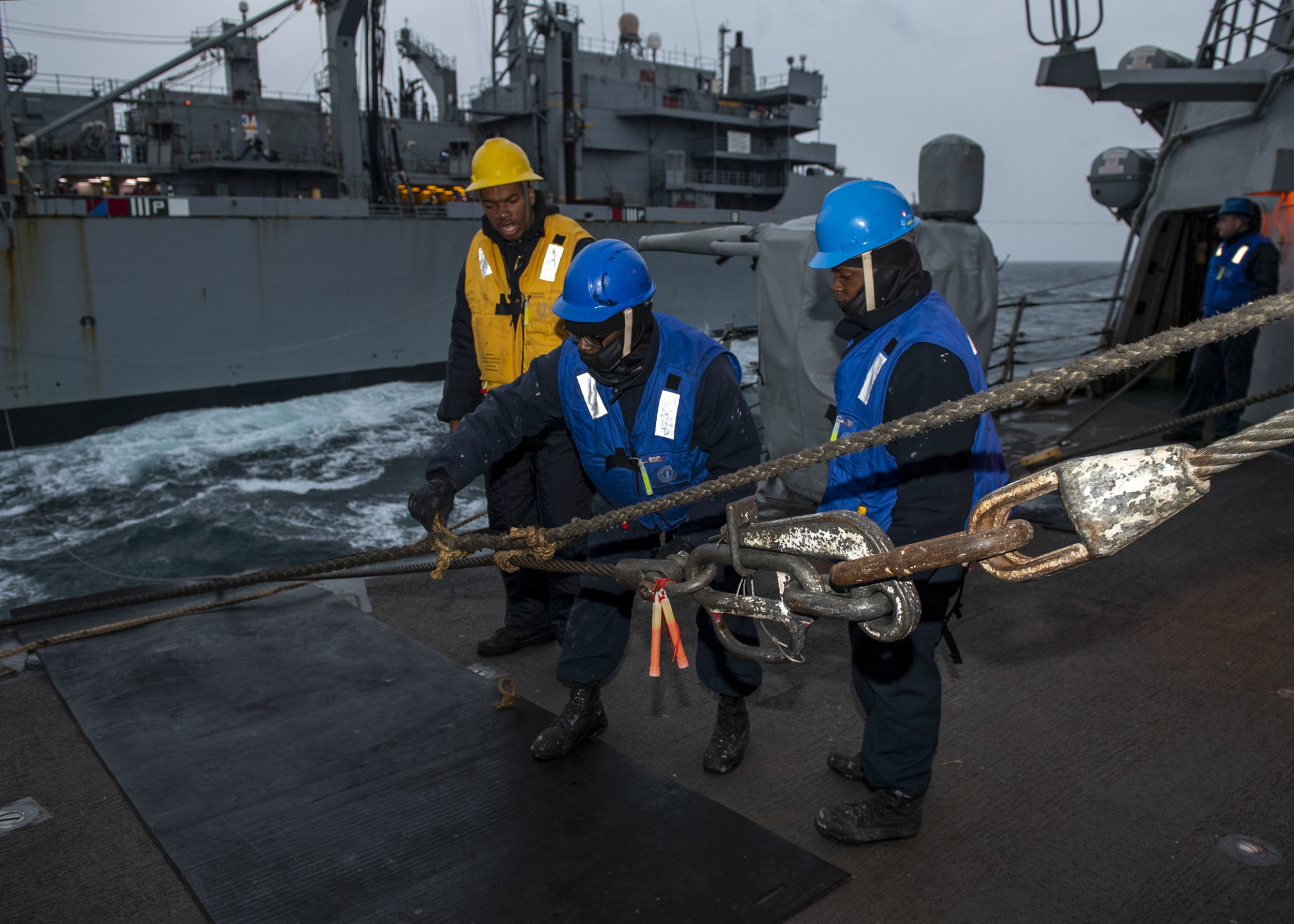 Boatswain’s Mate Seaman Floyd Davis, center, from Fredrick, Md., assigned to the Arleigh Burke-class guided-missile destroyer USS Mitscher (DDG 57), removes line from the high line during a replenishment-at-sea with Supply-class fast combat support ship USNS Supply (T-AOE-6), March 30, 2022.