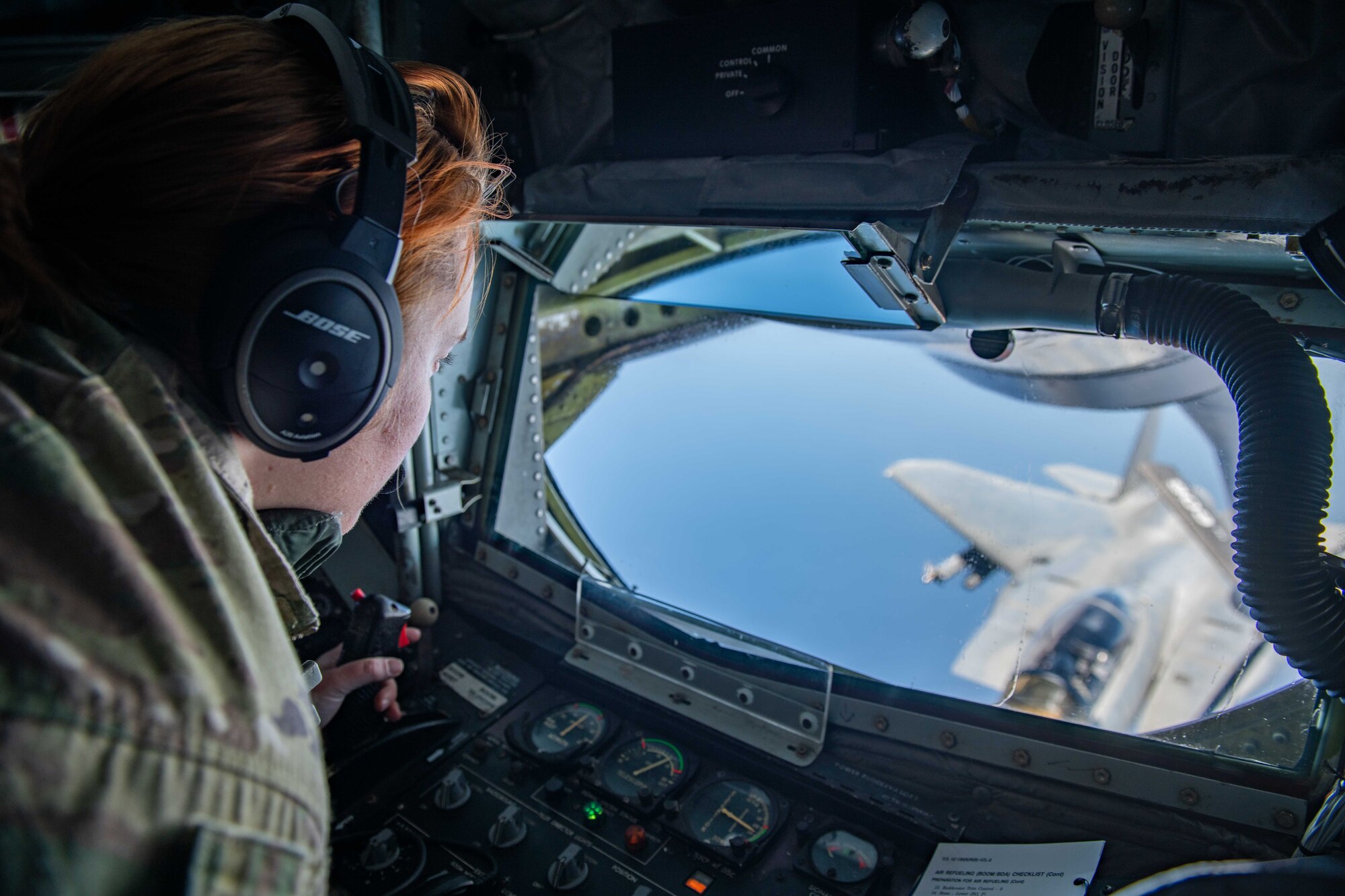 An airman watches as she refuels a fighter jet from the boom pod