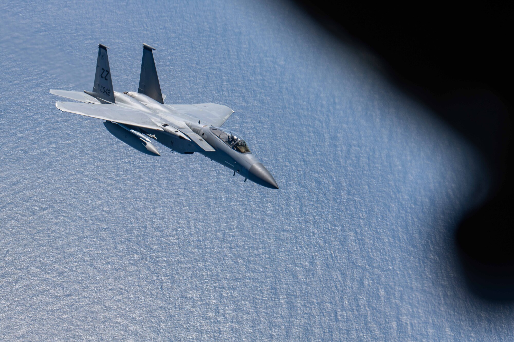 A fighter jet flies underneath a refueling plane over the ocean