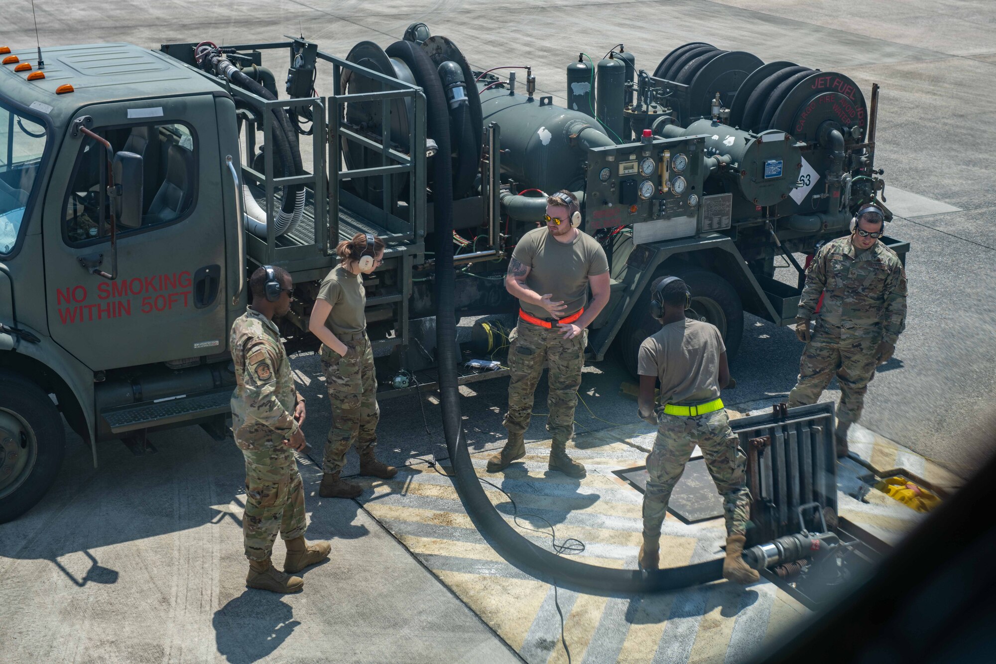 Airmen outside a plane refuel it with fuel from a truck