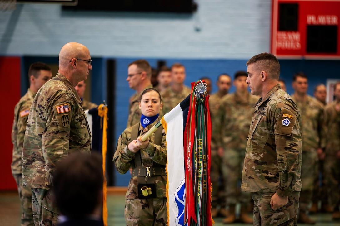 A soldier holds a flag between two other soldiers during a ceremony.