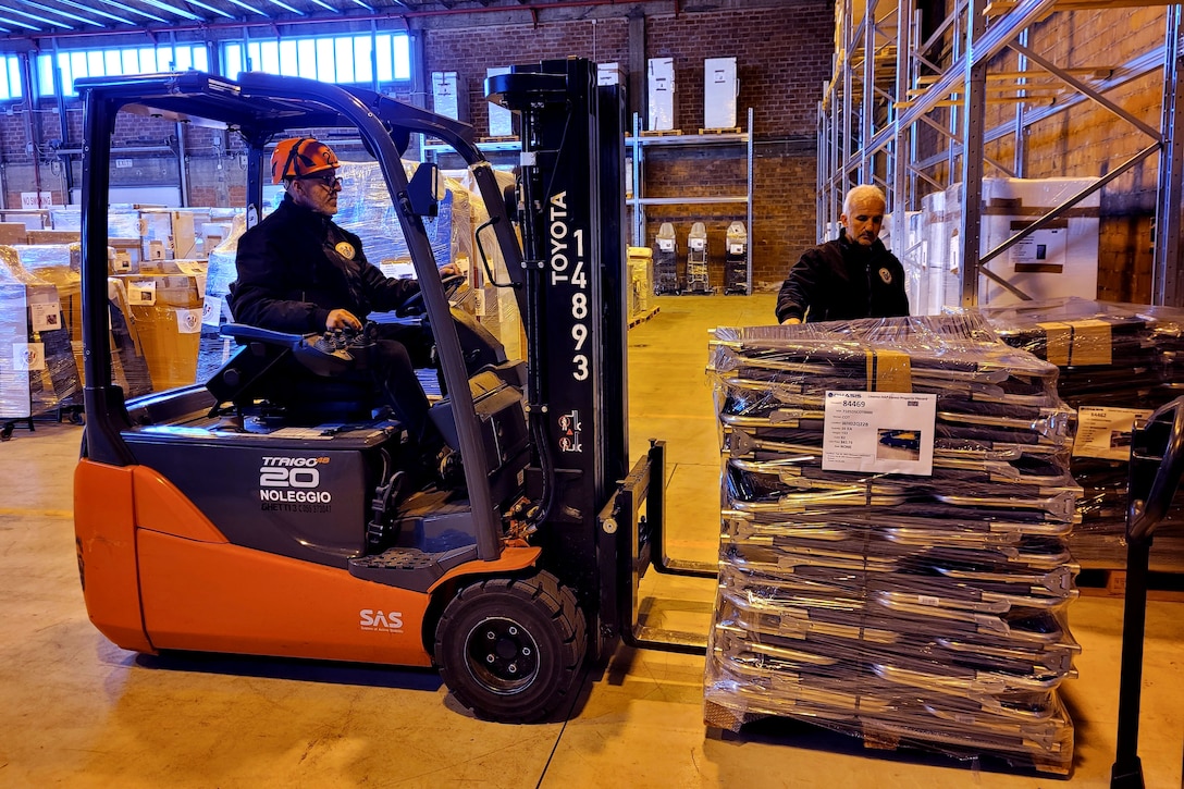 A man operates a forklift while another man assists with loading the pallet.