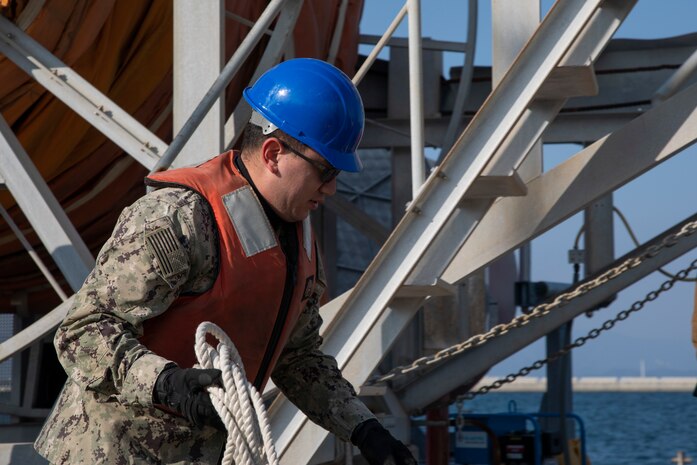 U.S. Navy Petty Officer Third Class Eric Hansen, a boatswain’s mate with Marine Corps Air Station Iwakuni’s harbor operation department, pulls in an oil boom at MCAS Iwakuni, Japan, Feb. 25, 2022. Boom reels are preventative equipment used to catch oil that may leak from vessels into the water. MCAS Iwakuni’s deep-water harbor plays an essential part in helping supply units on the air station with necessary equipment and helping support different vessels traveling through the Indo-Pacific region.