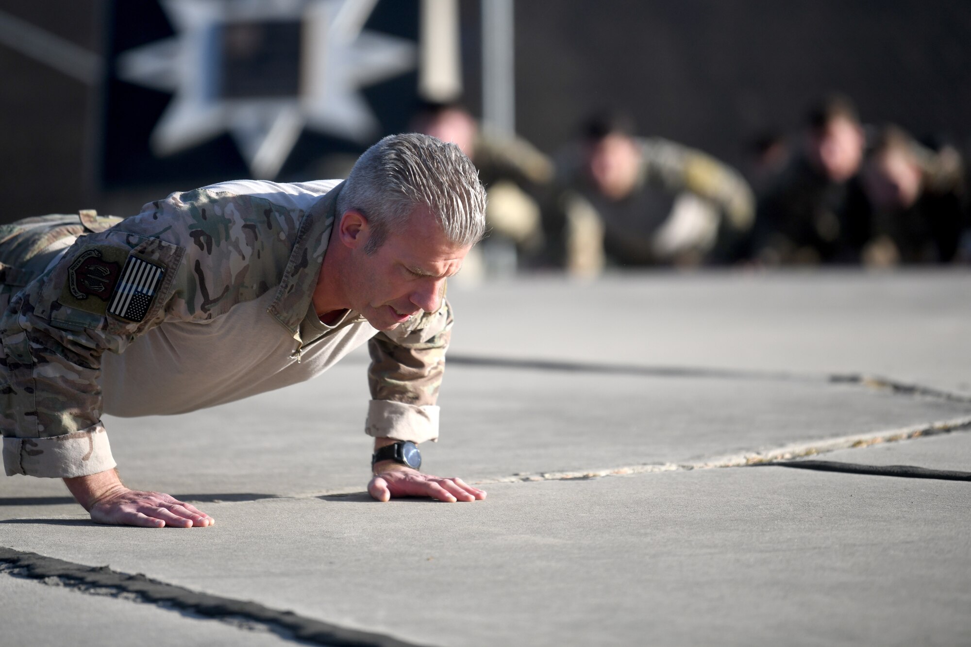U.S. Air Force Chief Master Sgt. Todd Popovic, Special Warfare Training Wing command chief, leads participants in Memorial pushups during a rededication ceremony in honor of U.S. Air Force Lt. Col. William Schroeder and U.S. Air Force Staff Sgt. Scott Sather at the SWTW training compound Joint Base San Antonio, Chapman Training Annex, Apr. 8, 2022.  The wing and echelon units hosted a two and one-half mile ruck march followed by Memorial pushups and the unveiling of refitted memorials in coordination with Gold Star families (U.S. Air Force photo by Brian Boisvert)