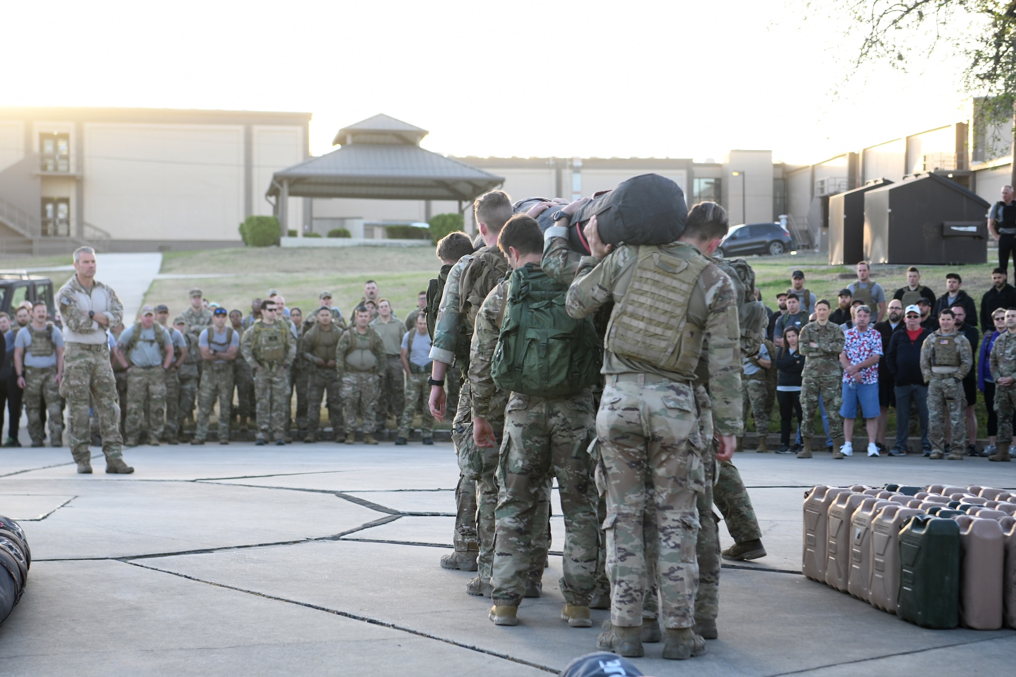 U.S. Air Force Chief Master Sgt. Todd Popovic, Special Warfare Training Wing command chief, left, watches as Special Warfare Trainees demonstrate the proper way to lift and carry a "charge" prior to a two and one-half mile ruck march in during a rededication ceremony in honor of U.S. Air Force Lt. Col. William Schroeder and U.S. Air Force Staff Sgt. Scott Sather at the SWTW training compound Joint Base San Antonio, Chapman Training Annex, Apr. 8, 2022.  The wing and echelon units hosted a two and one-half mile ruck march followed by Memorial pushups and the unveiling of refitted memorials in coordination with Gold Star families (U.S. Air Force photo by Brian Boisvert)