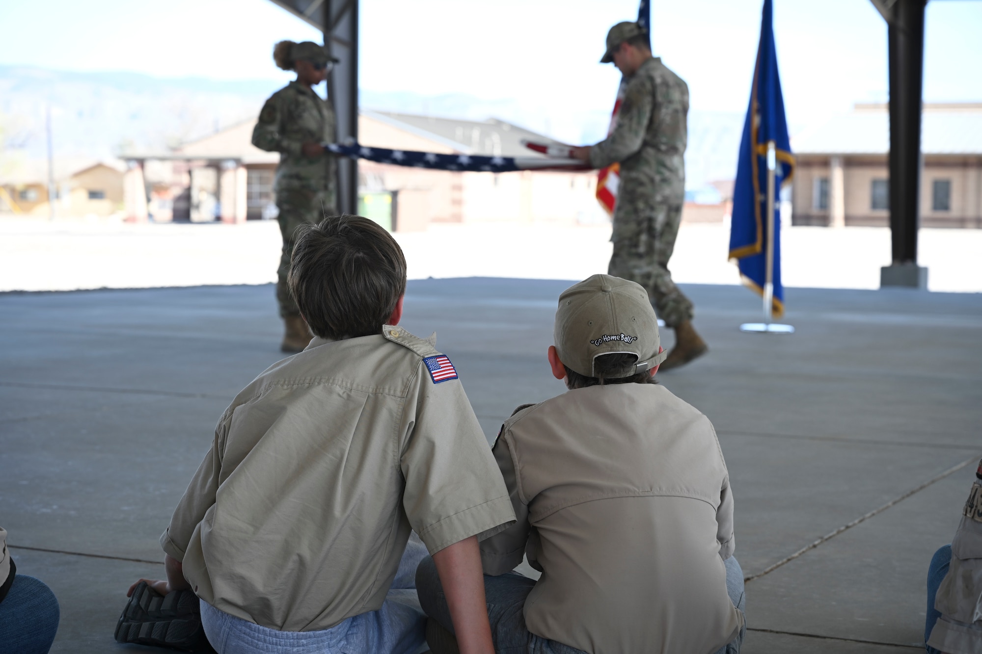 Two troops from Scout Troop BSA 4434 observe two Steel Talons Honor Guard members demonstrate a flag folding technique, April 1, 2022, on Holloman Air Force Base, New Mexico. Engaging with the external community allows Holloman to showcase its capabilities and gives the public a better understanding of the 49th Wing’s mission. (U.S. Air Force photo by Airman 1st Class Antonio Salfran)