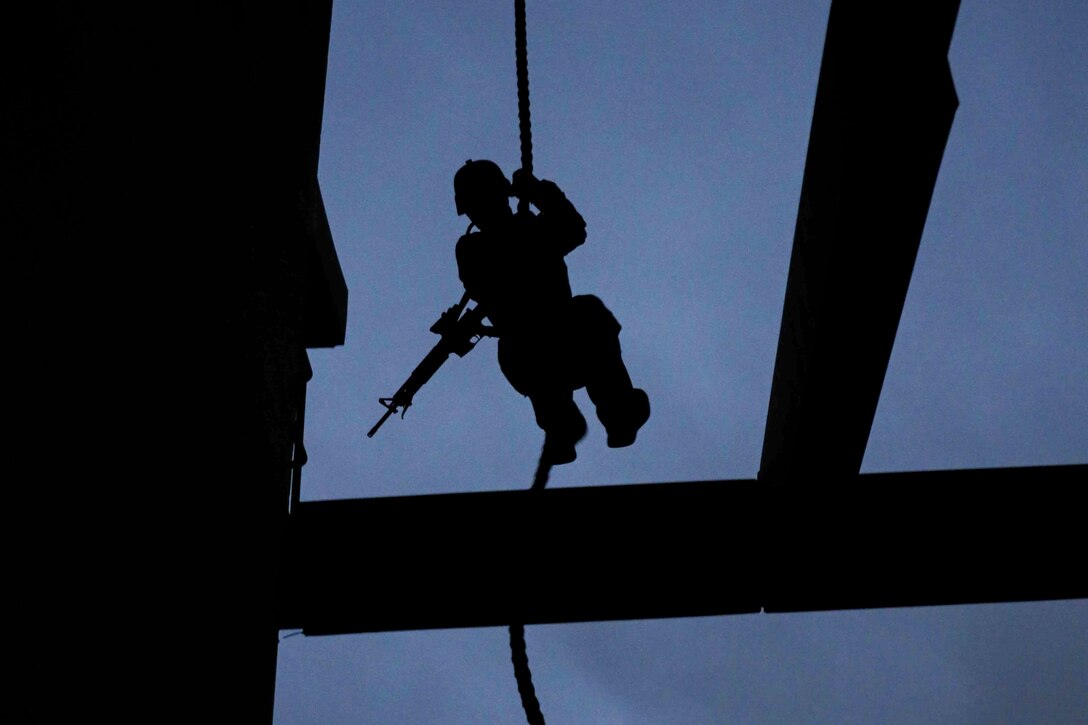 A Marine carrying a weapon fast-ropes as shown in silhouette.