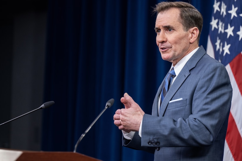 Pentagon Press Secretary John F. Kirby stands behind a lectern with an American flag at his back.