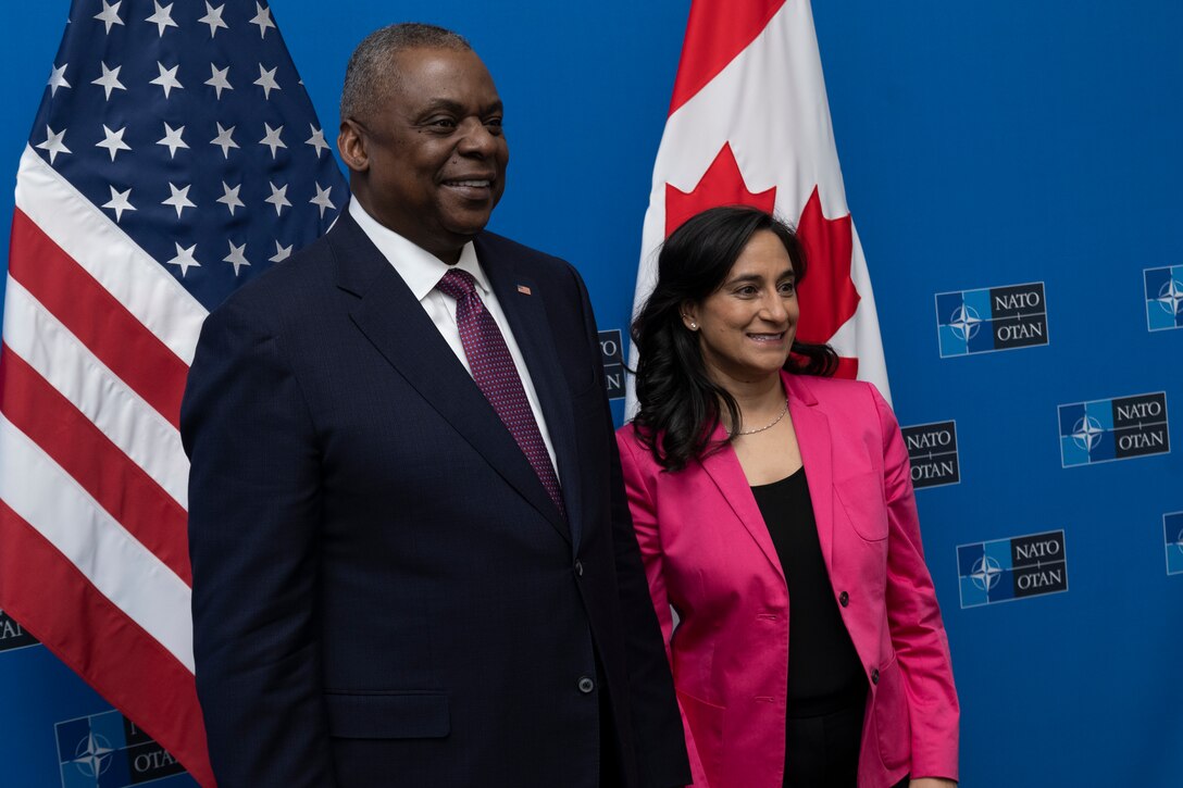 Secretary of Defense Lloyd J. Austin III stands with Canadian Defense Minister Anita Anand in front of flags.