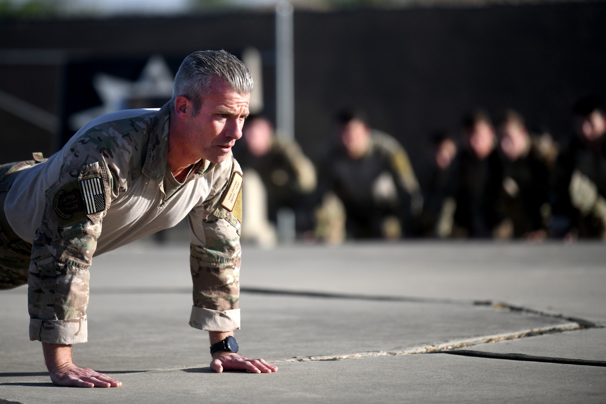 U.S. Air Force Chief Master Sgt. Todd Popovic, Special Warfare Training Wing command chief, leads participants in Memorial pushups during a rededication ceremony in honor of U.S. Air Force Lt. Col. William Schroeder and U.S. Air Force Staff Sgt. Scott Sather at the SWTW training compound Joint Base San Antonio, Chapman Training Annex, Apr. 8, 2022.  The wing and echelon units hosted a two and one-half mile ruck march followed by Memorial pushups and the unveiling of refitted memorials in coordination with Gold Star families (U.S. Air Force photo by Brian Boisvert)