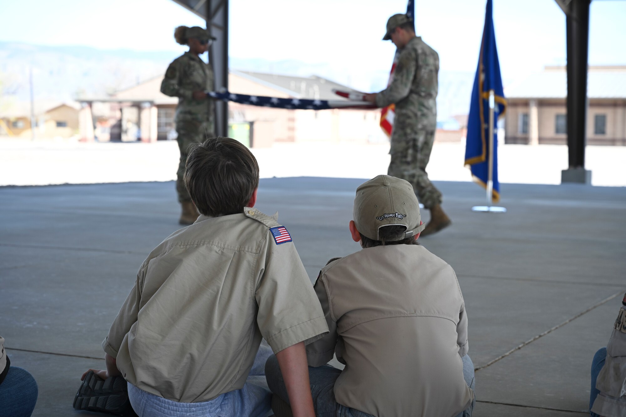 Two troops from Scout Troop BSA 4434 observe two Steel Talons Honor Guard members demonstrate a flag folding technique, April 1, 2022, on Holloman Air Force Base, New Mexico. Engaging with the external community allows Holloman to showcase its capabilities and gives the public a better understanding of the 49th Wing’s mission. (U.S. Air Force photo by Airman 1st Class Antonio Salfran)