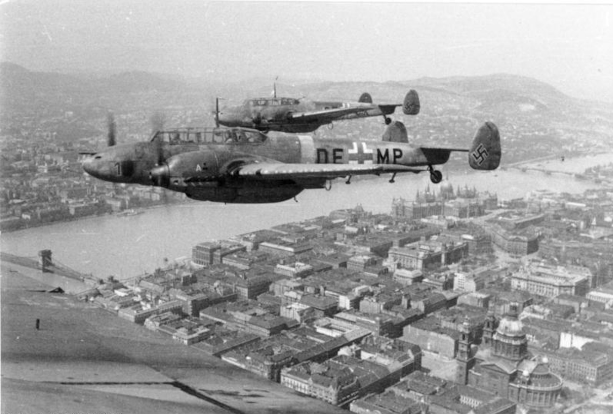 A pair of Messerschmitt Me-110 (also knowns as Bf-110) Zerstorer (Destroyer) fighters from the are pictured over Budapest, Hungary in 1944; the fuselage code of the aircraft nearest (DE+MP) indicates the aircraft were assigned to Ausbildungs Kommando Zerstorer, a training  unit for Hungarian air units operating the type (unit ID by Heikki Hyttinen).  Two Me-110s from Jagdgeschwader 400 at Brandis Airfield, Germany were involved in the fateful aerial encounter of 13 April 1945 near Hainichen involving P-47s of the 406th Fighter Squadron, 371st Fighter Group and Capt. William T. Bales, Jr.  (Deutsch Bundesarchiv, via Wikipedia)