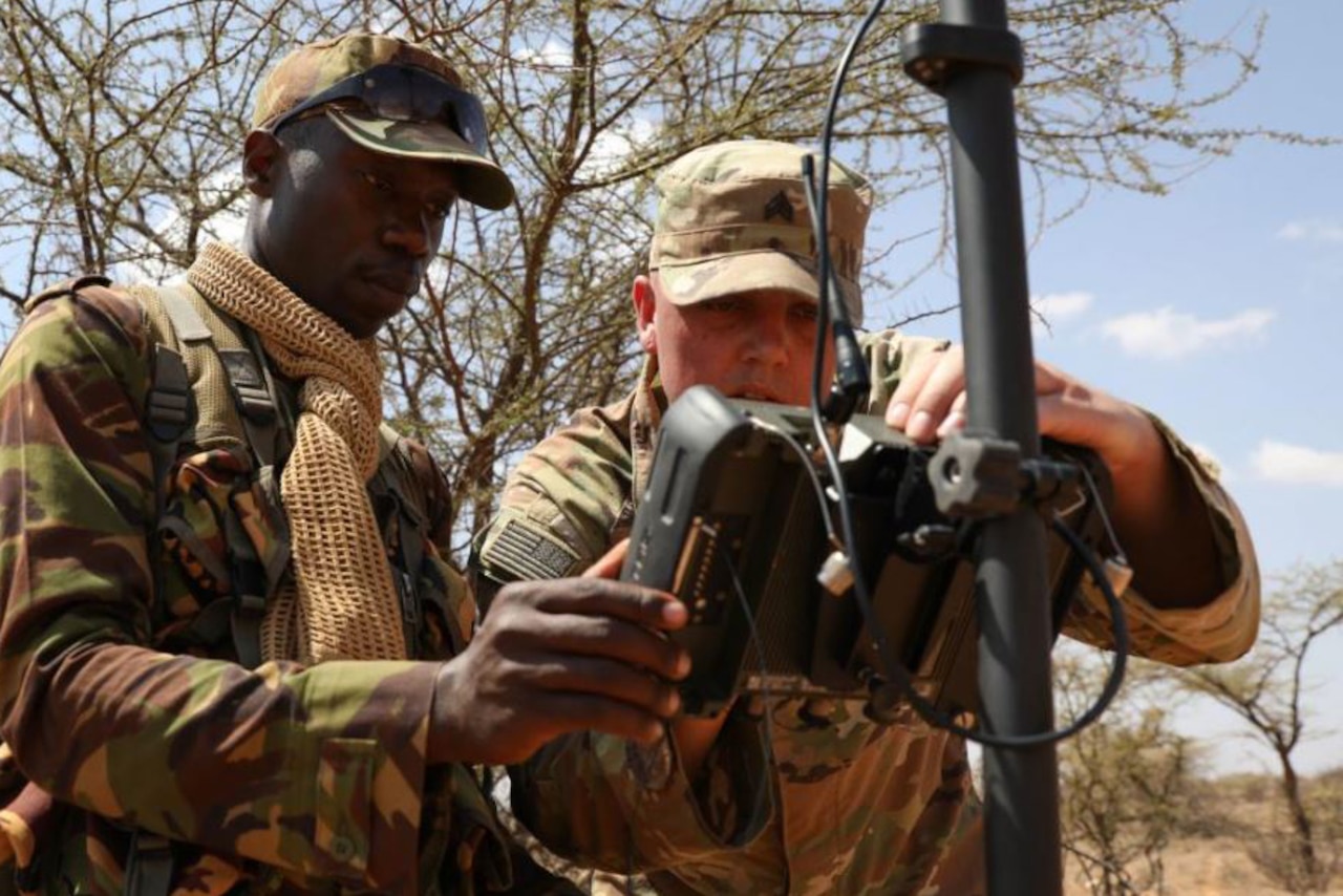 Two soldiers work together with survey equipment.