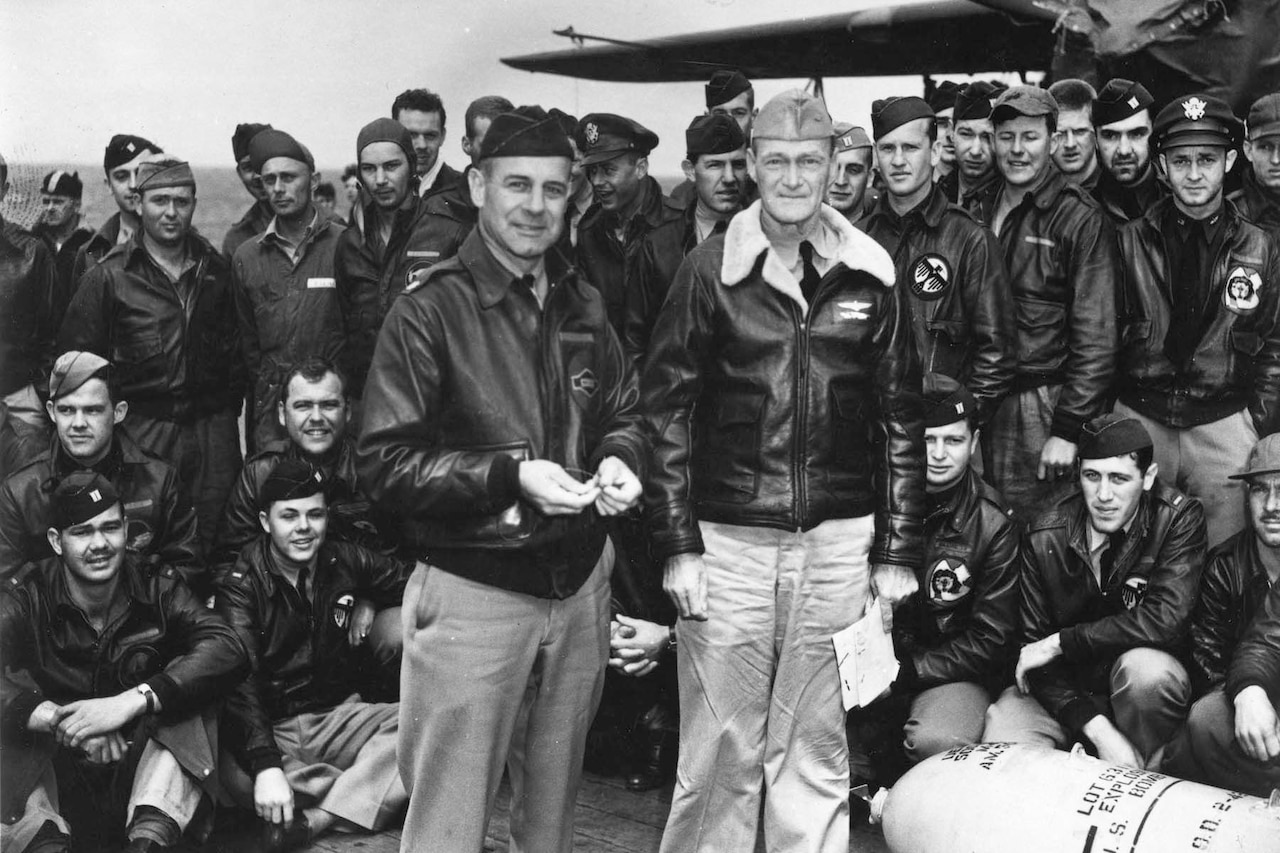 Two men stand in the front of a group of men posing for a photo on the deck of a ship.