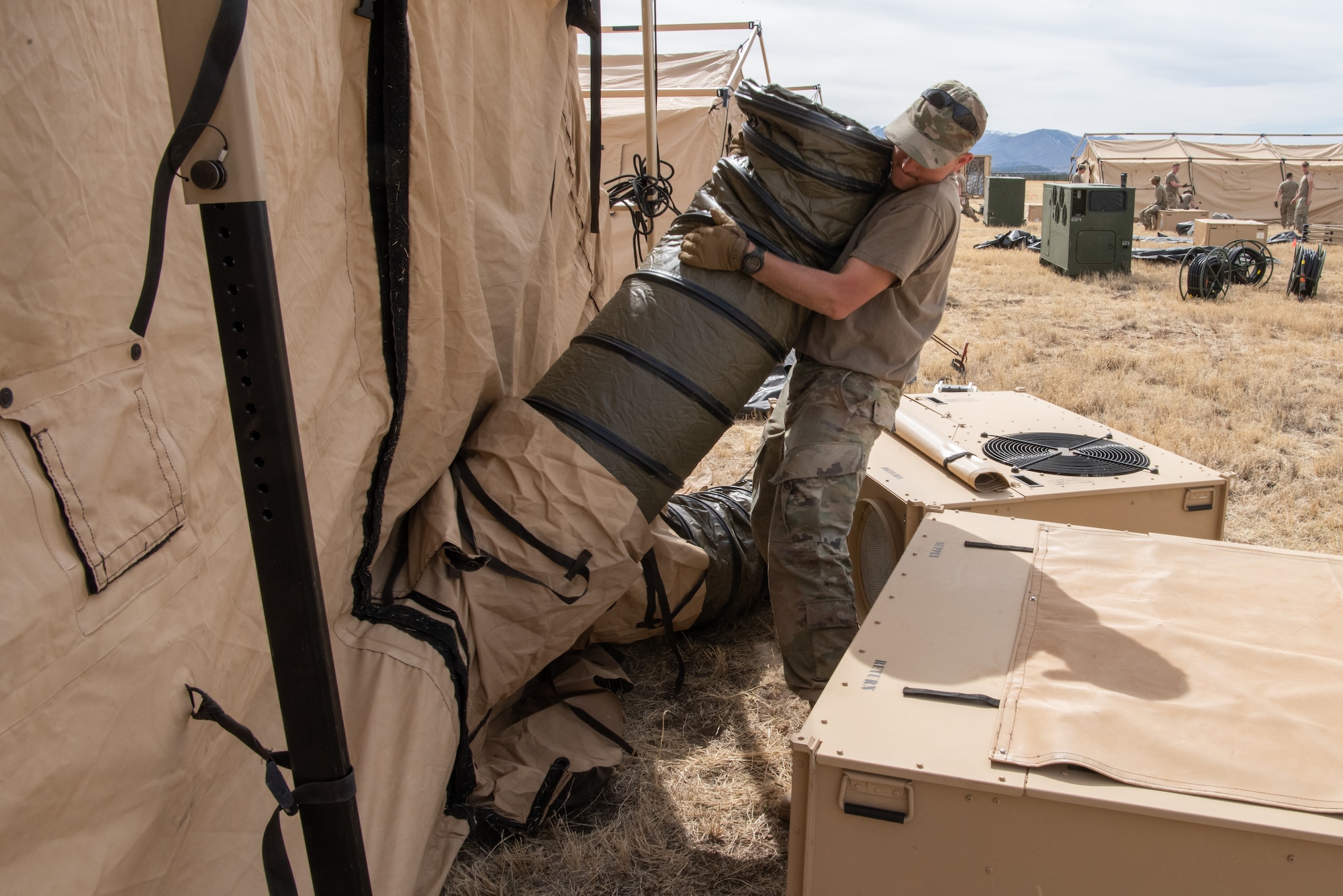 U.S. Air Force Senior Airman Robert Ditsch, 27th Special Operations Civil Engineer Squadron heating, ventilation and air conditioning journeyman, connects an air duct from a Utilis TM-80 tent to an air conditioning unit during the Full Mission Profile 22-3 exercise at Sierra Blanca Regional Airport, New Mexico. (U.S. Air Force photo by Airman 1st Class Alexis Sandoval)