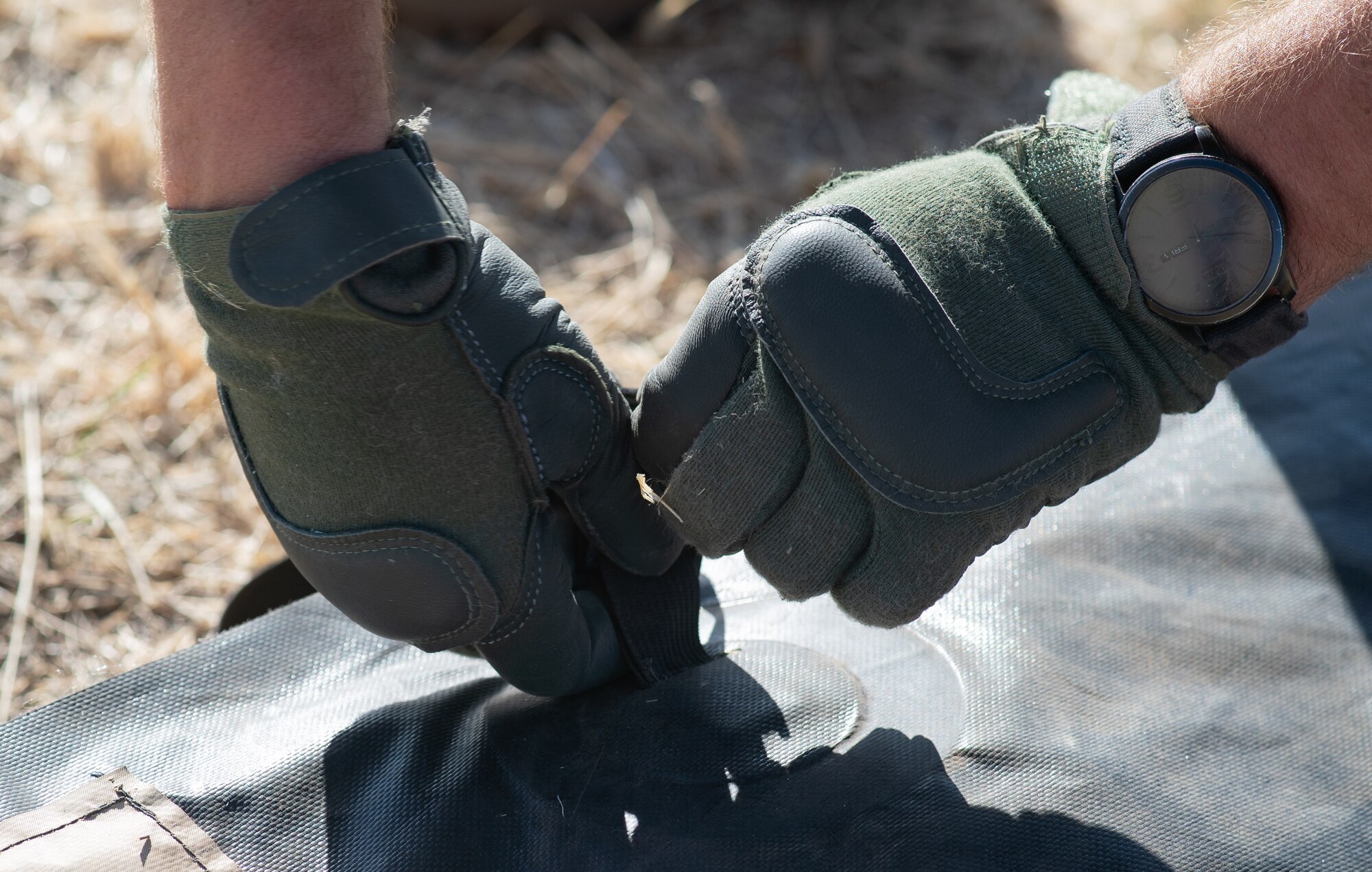 Two gloved hands cinch down a strap closing the fabric cover of a Utilis TM-60 tent during 27th Special Operations Mission Support Group, Detachment 1 Mission Sustainment Team 2's Full Mission Profile 22-3 exercise. (U.S. Air Force photo by Senior Airman Christopher Storer)