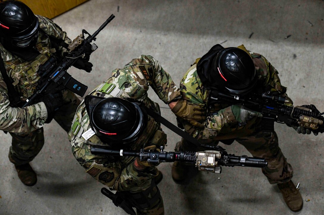 A look above at three airmen moving through an area holding weapons.