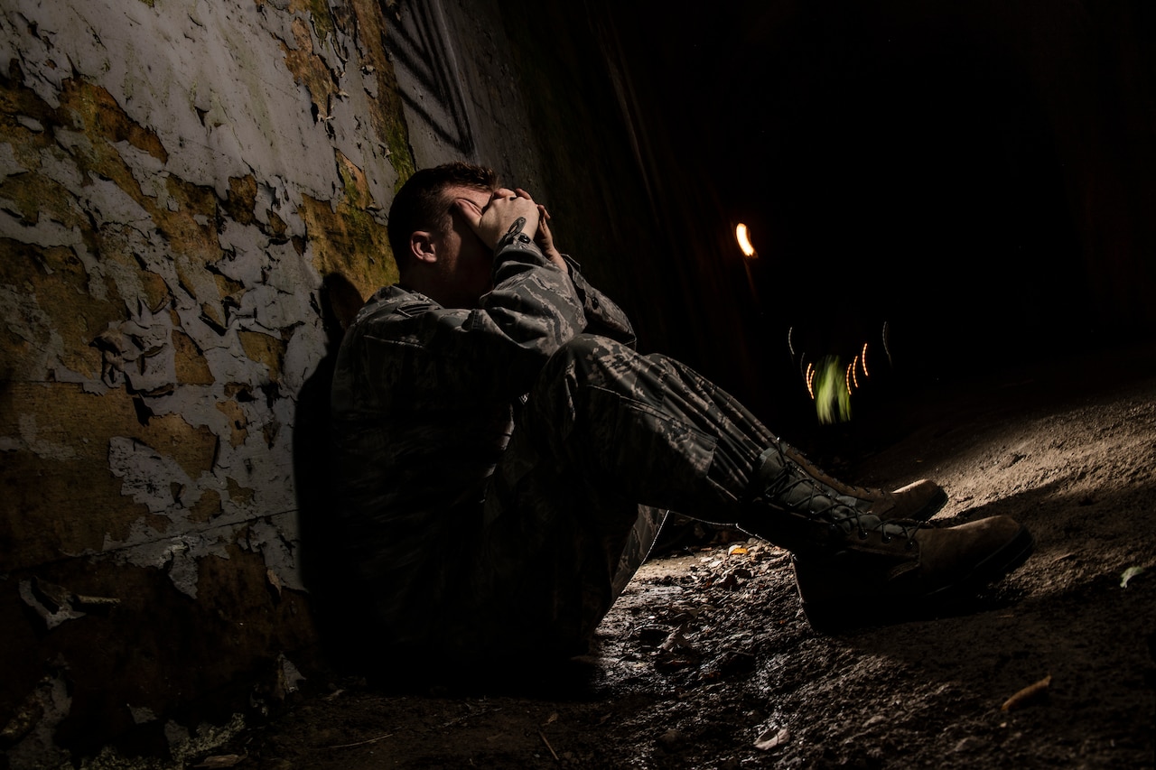 A service member sits with his hands on his face in the dark.
