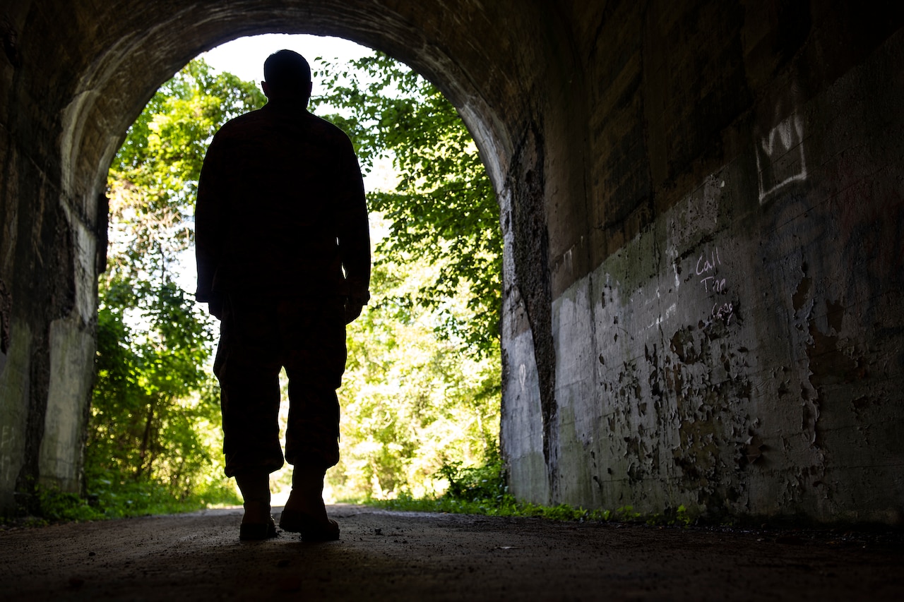 A service member’s silhouette stands near the entrance of a dark tunnel.