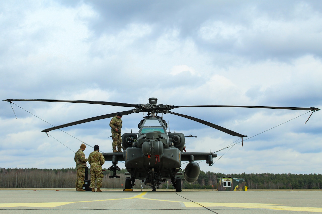 Three soldiers tend to a parked helicopter.