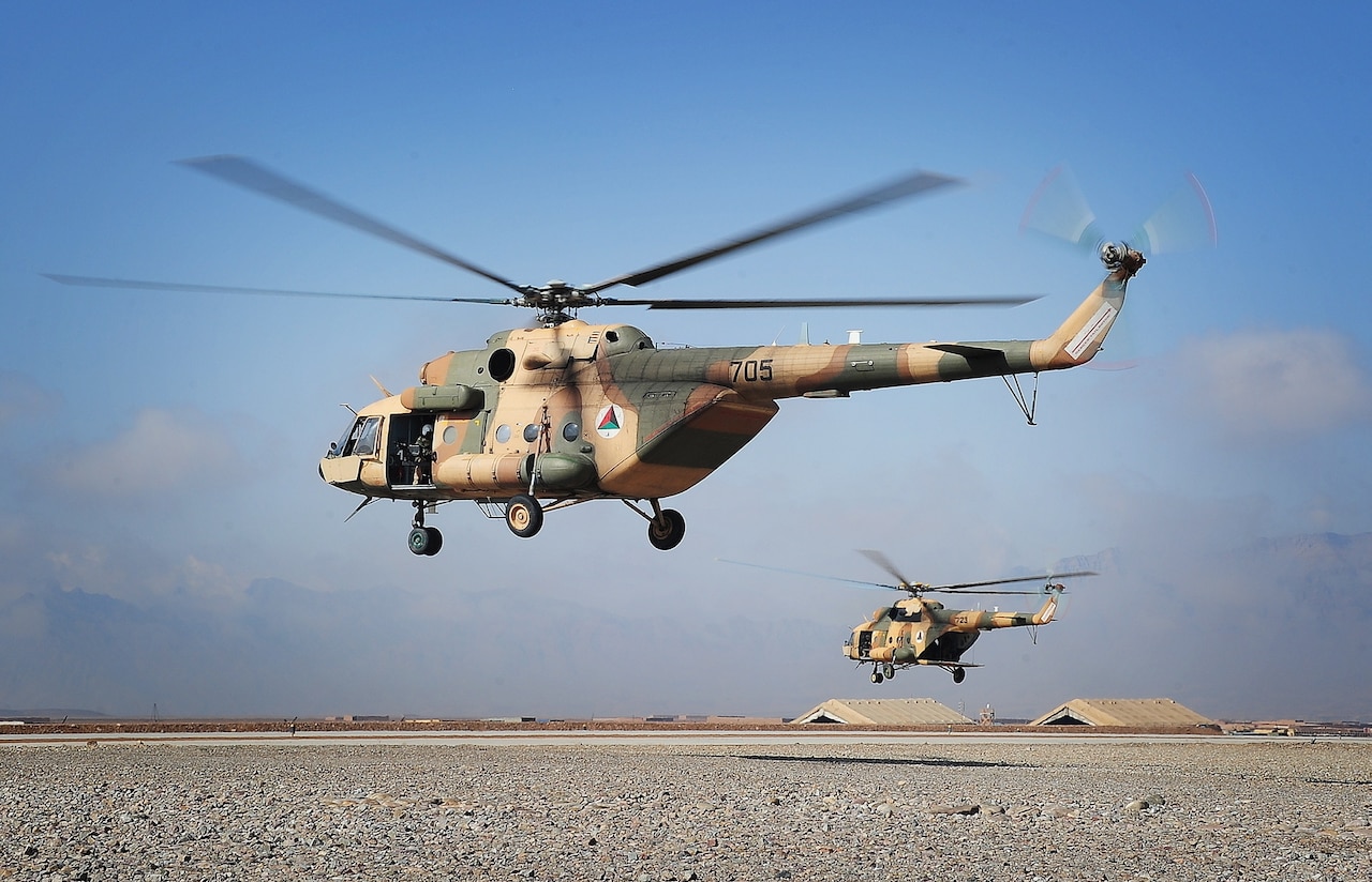 Two helicopters fly across a desert landscape.