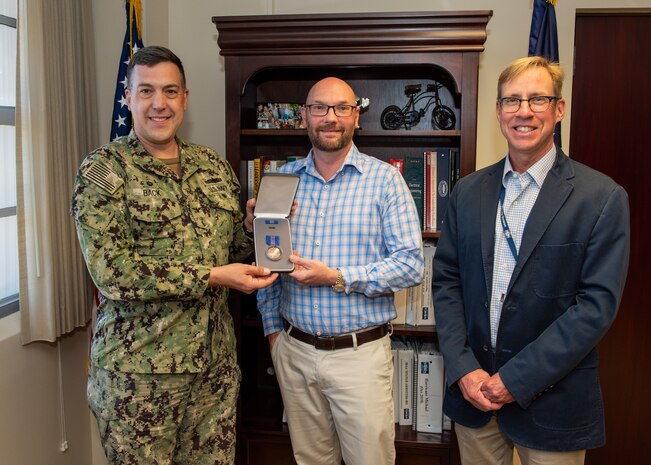 (left) Capt. David Back, Naval Surface Warfare Center commanding officer and (right) Dr. Peter Adair, NSWC PCD technical director present Stephen (Rusty) Weathers, NSWC PCD Airborne Mine Neutralization System lead systems engineer with the Department of the Navy’s Meritorious Civilian Service Award on March 28. Weathers is responsible for all aspects of engineering and serves as the subject matter expert for the AMNS program and has been at NSWC PCD since 2012. (U.S. Navy photo by Anthony Powers)