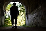 A service member’s silhouette stands near the entrance of a dark tunnel.