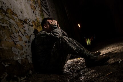 A service member sits with his hands on his face in the dark.