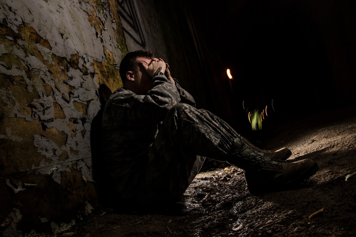 A service member sits with his hands on his face in the dark.
