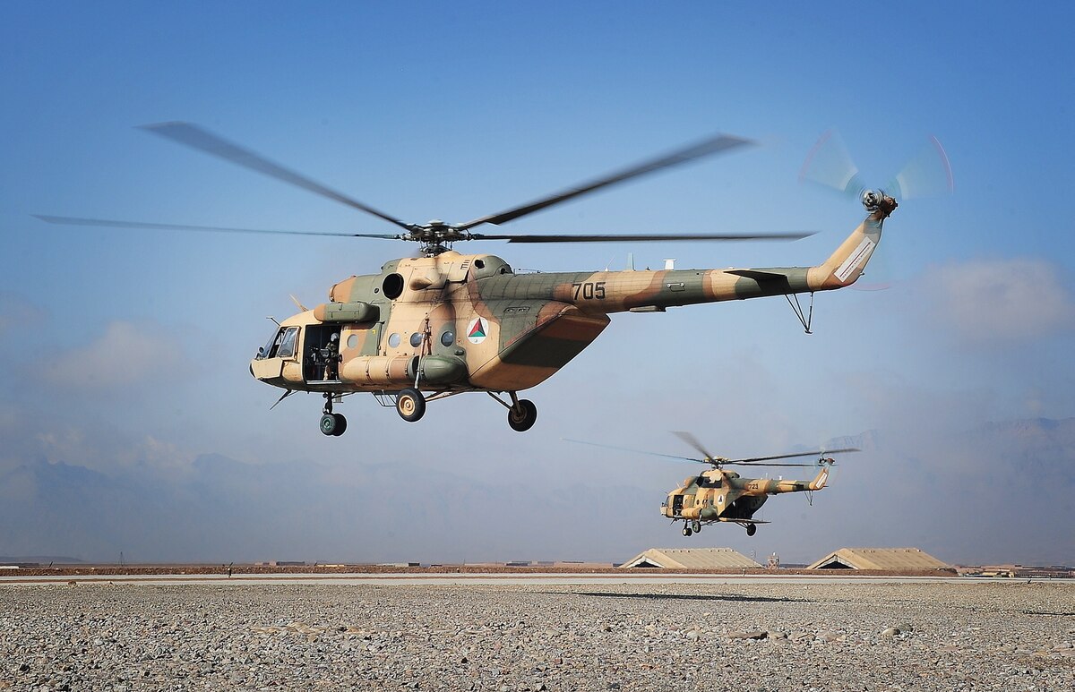 Two helicopters fly across a desert landscape.