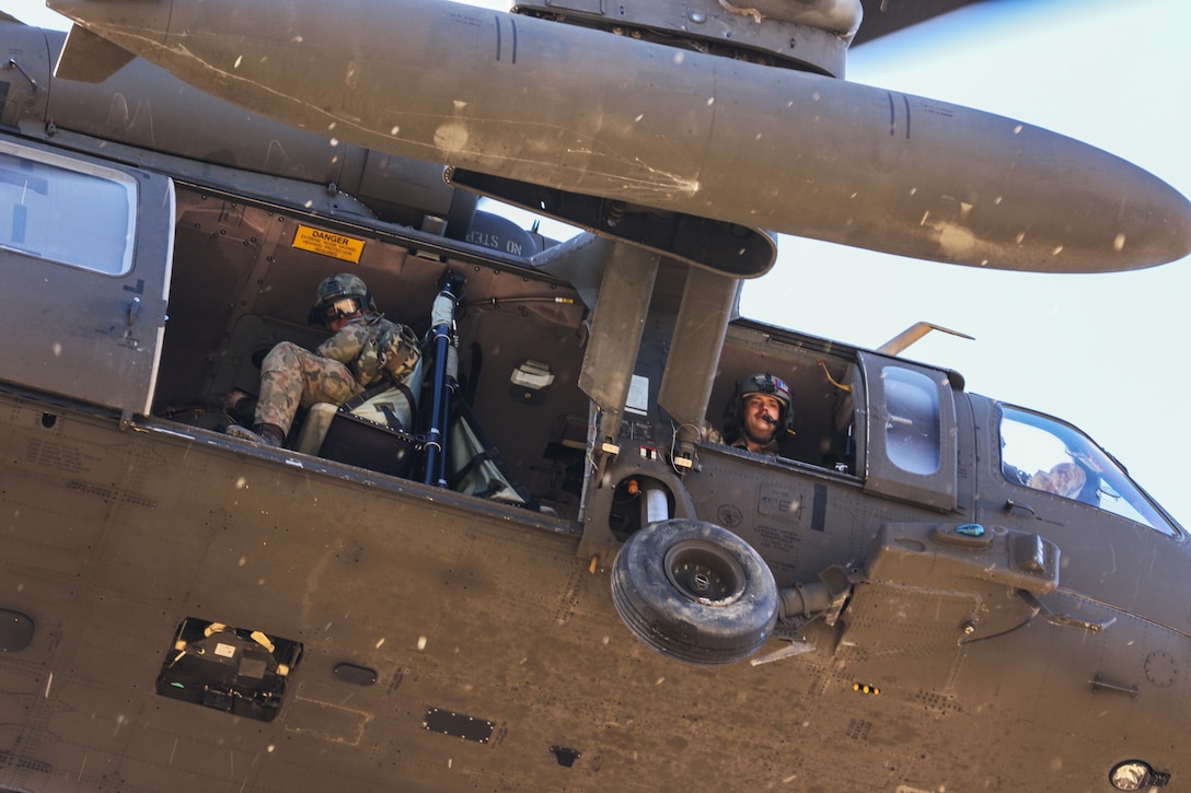 Two paratroopers in an actively flying helicopter look down from their seats.