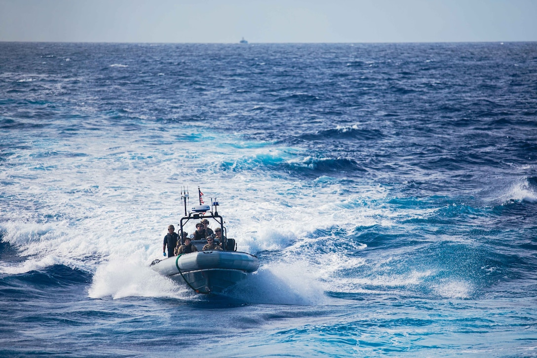 Coast Guardsmen and sailors pilot an inflatable boat through the water.