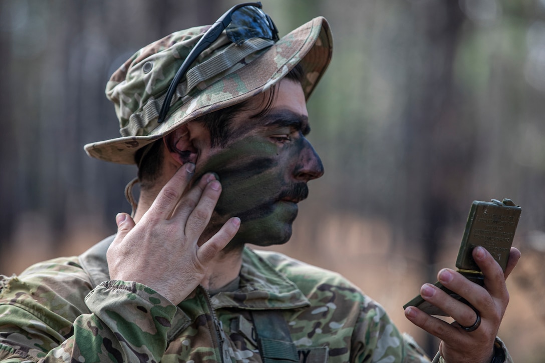 A soldier puts camouflage paint on his face.